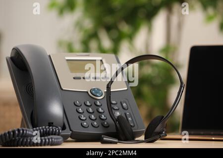 Cuffia, telefono desktop e computer portatile sul tavolo al coperto. Concetto di hotline Foto Stock