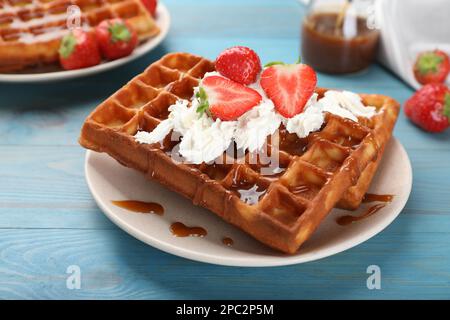 Deliziosi waffle belgi con fragole, panna montata e salsa al caramello su tavola di legno turchese, primo piano Foto Stock