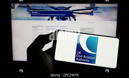Persona che tiene il cellulare con il logo della British Regulator Civil Aviation Authority (CAA) sullo schermo di fronte alla pagina web. Messa a fuoco sul display del telefono. Foto Stock