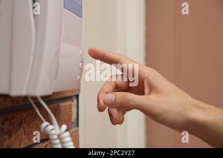 Uomo che preme il pulsante sul pannello interfono all'interno, primo piano Foto Stock