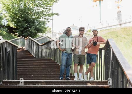 tutta la lunghezza dei turisti interrazziali felici con la mappa della città in piedi sulle scale in città, immagine di scorta Foto Stock