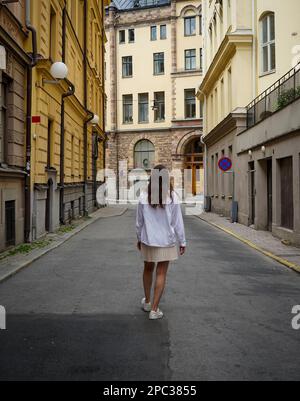 Vista posteriore della donna che cammina sulla strada tra gli edifici della città Foto Stock