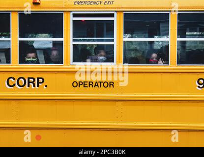 Bambini che indossano maschere durante la guida di Covid un autobus scolastico Foto Stock