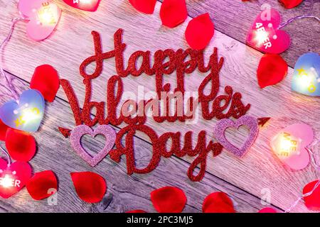 Un'immagine di una formazione a forma di cuore rosso vibrante di petali di rosa giacenti su uno sfondo bianco con le parole 'buon San Valentino' al centro Foto Stock