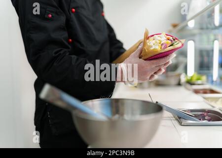 Il cuoco cucina pita souvlaki sandwich in tradizionale greco fast food ristorante. Concetto di cucina globale Foto Stock