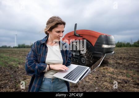 Un agricoltore con tablet digitale controlla un trattore autonomo in un'azienda agricola intelligente Foto Stock