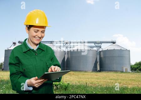 Donna ingegnere con un tablet digitale su un background di silos agricoli per la produzione di biocarburanti Foto Stock