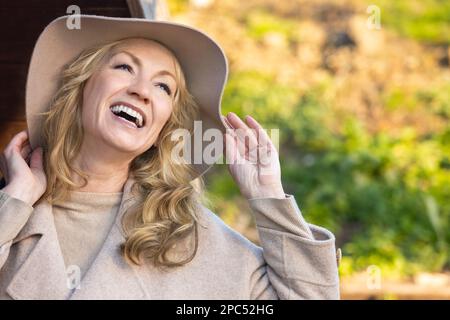 Attraente felice sorridente elegante donna di mezza età con denti perfetti all'esterno indossando un cappello Foto Stock