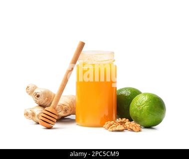 Miele in vaso aperto con noci, lime e zenzero su fondo bianco. Alimenti sani. Miele in un vaso di vetro con il bastone di miele sull'isolamento Foto Stock