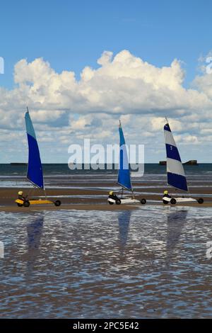 Arromanches, Francia - 14 2012 ottobre: Tre persone che hanno una gara amichevole di sabbia yachting su Gold Beach in Normandia. Sullo sfondo, possiamo ancora se Foto Stock