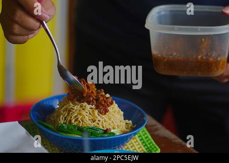 Un tipo ha messo la guarnizione su mie Ayam o sulle tagliatelle indonesiane del pollo con brodo. con brodo servito in ciotola con salsa di peperoncino. Foto Stock