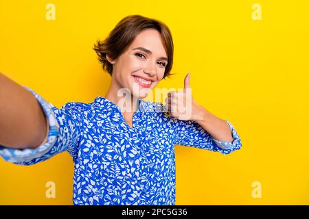 Ritratto fotografico di bella giovane donna selfie fotocamera anteriore mostra pollice su 5g vestito elegante abito da stampa isolato su sfondo giallo Foto Stock