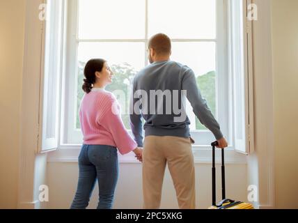 Vista posteriore di una coppia di viaggiatori in piedi con Suitcase in hotel Foto Stock