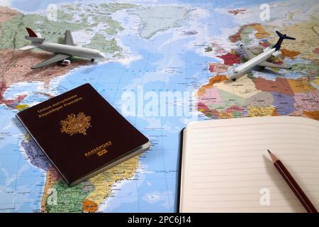 Mappa del mondo con su di esso, due aerei giocattolo, un passaporto francese e una penna a sfera sulla parte superiore di un blocco note aperto. Foto Stock