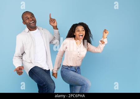 Overjoyed uomo nero di mezza età e giovane donna che si divertono insieme e ballano su sfondo blu, copia spazio Foto Stock