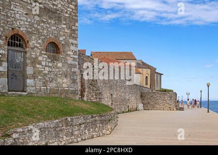 I turisti che camminano sul lungomare lungo le antiche mura della città di Poreč / Parenzo, località balneare sul mare Adriatico, Istria County, Croazia Foto Stock