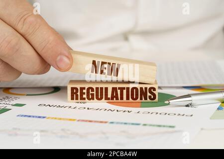 Concetto aziendale. Sulla tabella sono le tabelle di affari e i diagrammi nelle mani di un blocco di legno con l'iscrizione - nuovo regolamento Foto Stock