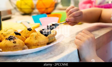 Capretto che decorano i muffin fatti in casa alla vaniglia con guarnizione al cioccolato. Foto Stock