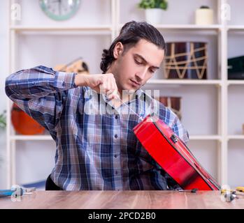 Il giovane bello repairman riparazione di chitarra Foto Stock