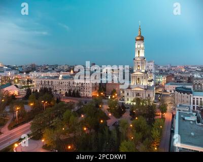 Veduta aerea della Cattedrale della Dormizione con cupola dorata e campanile sul cielo blu del tramonto alle luci serali del centro di Kharkiv, Ucraina. Foto Stock