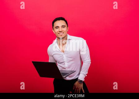 Immagine di un giovane uomo d'affari allegro in possesso di un orologio e utilizzando un computer portatile isolato su sfondo rosso Foto Stock