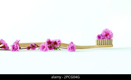 Spazzolino da denti in legno con setole naturali decorato con piccoli fiori isolati su sfondo bianco. Concetto creativo di dentifricio floreale Foto Stock