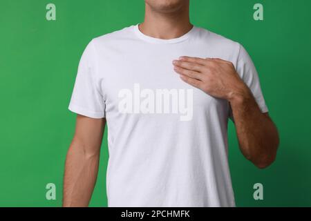 Uomo che tiene la mano vicino al petto su sfondo verde, primo piano Foto Stock