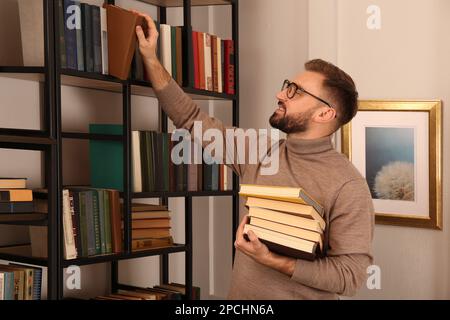 Giovane uomo che sceglie i libri sullo scaffale nella biblioteca domestica Foto Stock