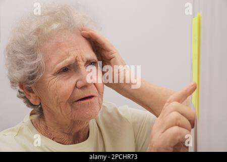 Donna anziana che guarda la nota di promemoria al chiuso. Compromissione della memoria correlata all'età Foto Stock