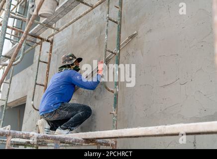 Lavoratore di costruzione con una cazzuola lunga per intonacare il muro a mano in cantiere. Foto Stock