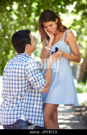 Dite di sì... Un giovane che si inginocchia nel parco e chiede alla sua ragazza di sposarlo. Foto Stock