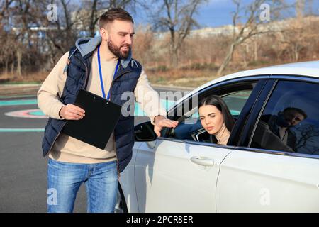 Istruttore vicino all'auto con una giovane donna durante l'esame in pista. Scuola guida Foto Stock