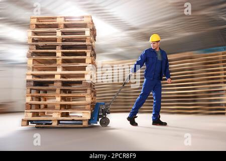 Operatore che sposta pallet in legno con carrello elevatore a forche manuale in magazzino Foto Stock