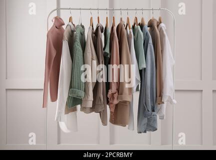 Rack con eleganti abiti da donna vicino a una parete luminosa Foto Stock