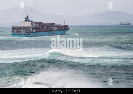 Una gigantesca nave da carico che naviga attraverso il mare del pacifico con onde che si infrangono al largo della costa della Nuova Zelanda. Foto Stock