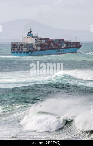 Una gigantesca nave da carico che naviga attraverso il mare del pacifico con onde che si infrangono al largo della costa della Nuova Zelanda. Foto Stock