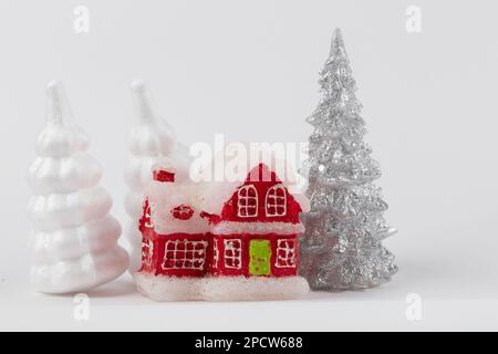 Scena di Natale, villaggio di dacha in miniatura. Case rosse di Natale, cervi e abeti innevati su sfondo bianco. Decorazioni moderne e festose. Foto Stock