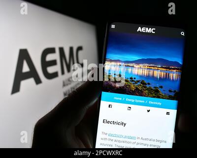 Persona che tiene un telefono cellulare con il sito web della Commissione australiana del mercato dell'energia (AEMC) sullo schermo con il logo. Messa a fuoco al centro del display del telefono. Foto Stock