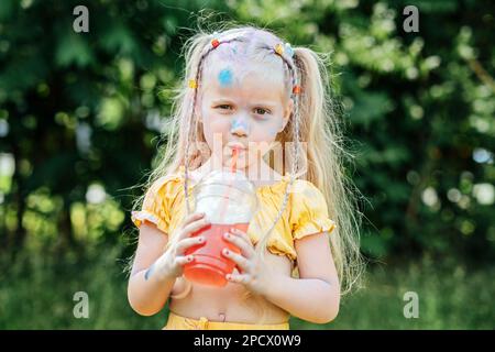 Ritratto all'aperto della bambina grisy Funny con due ponytail bevande limonata dolce zuccherato, frizzante il giorno d'estate. Zucchero in bevande per bambini Foto Stock