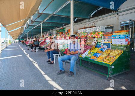 Vari venditori di uomini pazientemente in attesa di clienti di fronte alle loro bancarelle. Al mercato locale di frutta, verdura, prodotti ad Abu Dhabi, Emirati Arabi Uniti Foto Stock