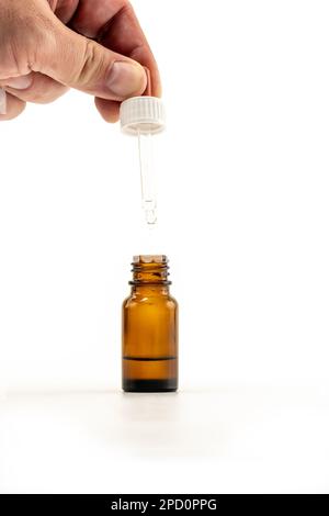 Foto di primo piano di persona che dispensa gocce mediche - gocciolando verticalmente in una bottiglia marrone da uno spuit Foto Stock