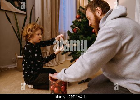 Zenzero padre e figlio in abbigliamento casual decorazione albero di Natale in accogliente soggiorno Foto Stock