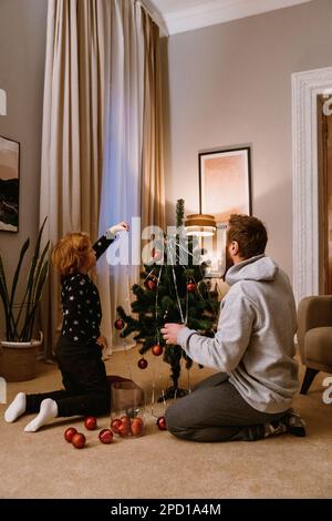 Zenzero padre e figlio in abbigliamento casual decorazione albero di Natale in accogliente soggiorno Foto Stock