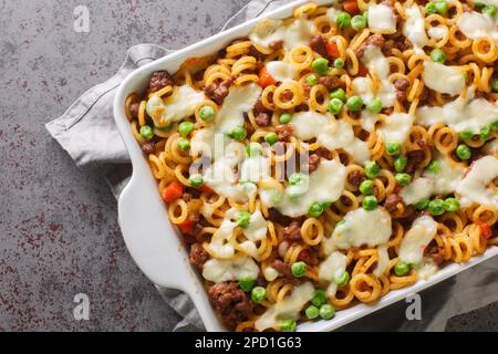 Pasta italiana anelli al forno con pomodori, formaggio, carne tritata, piselli verdi, carote e sedano primo piano in un piatto da forno sulla tavola. Orizzontale in alto v Foto Stock