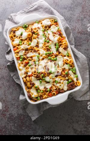 Casseruola di pasta anelli con pomodori, formaggio, carne tritata, piselli verdi, carote e sedano primo piano in una teglia da forno sulla tavola. Vista dall'alto verticale fr Foto Stock