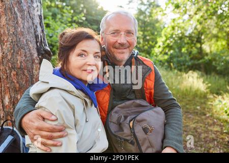 Ritratto di sorridente coppia anziana seduta con zaino in foresta durante le vacanze estive Foto Stock