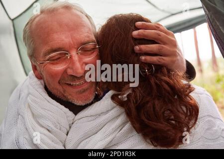 Felice uomo anziano abbracciando la donna mentre avvolto in coperta all'interno tenda a foresta Foto Stock