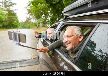 Felice uomo anziano che porta il selfie attraverso lo smartphone con un amico mentre viaggia in auto durante le vacanze Foto Stock