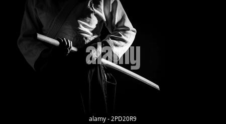 Una persona in hakama nero in posa di combattimento con la spada di legno bokken in bianco e nero. Profondità di campo bassa. SDF. Foto Stock