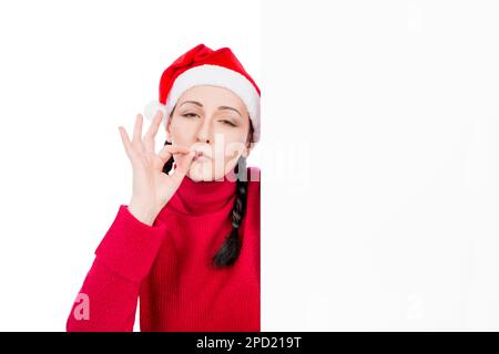 Ragazza a Santa Hat fare ok gesto positivo da dietro bianco pubblicità cartello pannello isolato su uno sfondo bianco. Concetto di vendita. Foto Stock